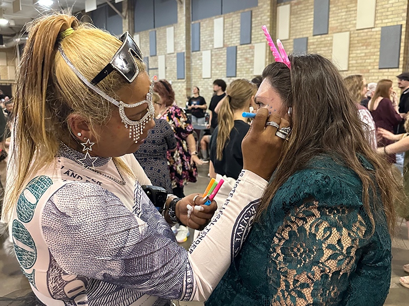 Woman adding pretty face painting details to a female student
