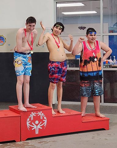 Students standing on the first, second, and third place stands for swimming in the 2023 Special Olympics Area Games